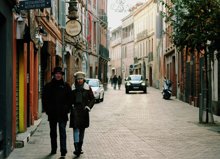 two people walking down an alley way next to parked cars