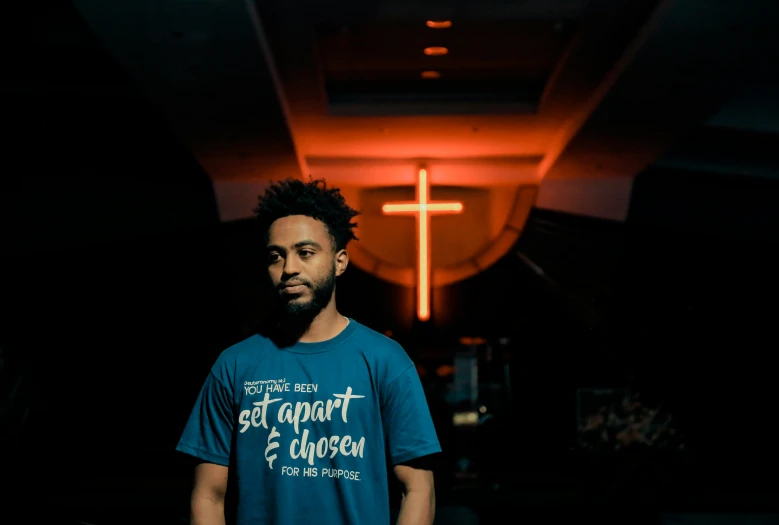 a man in a t - shirt is standing against a dark background