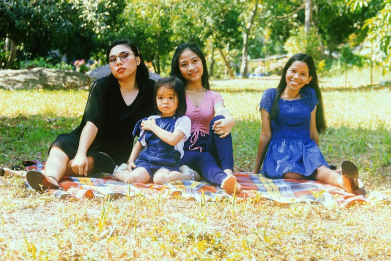 the people are sitting in the grass while one of them is holding a baby