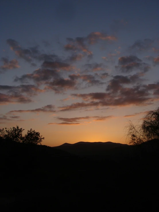 the sun is rising over a hill near a wooded area