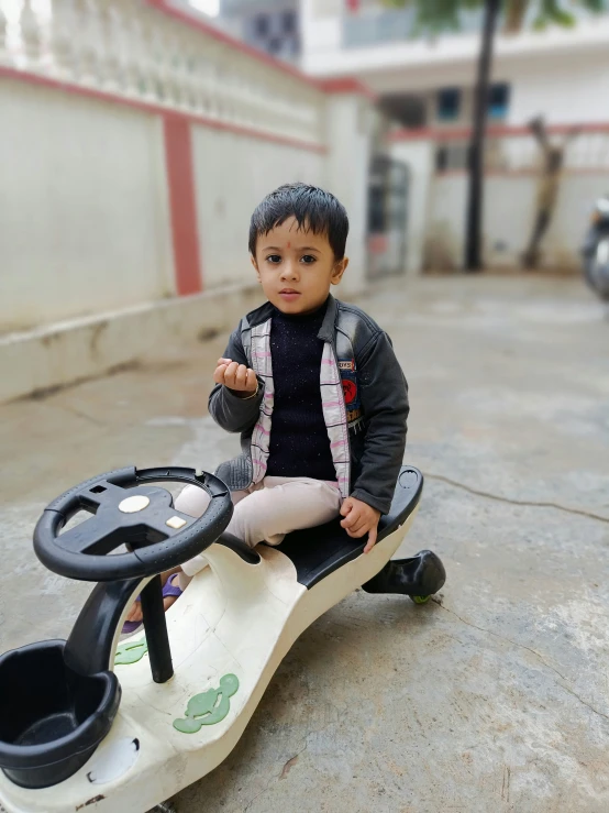 a little boy sitting on a motorized car on the sidewalk