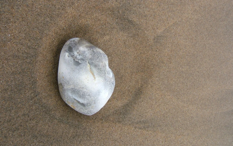 a rock laying on top of a sandy beach