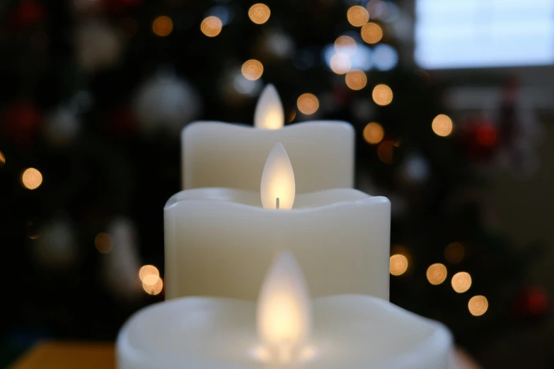 four lit candles on table with a christmas tree in background