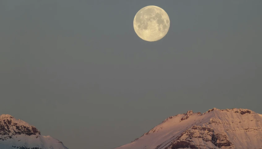 the full moon shines brightly as it rises above some snow covered mountains