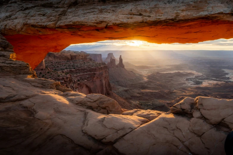 the sun peeking through a cave that has a view of canyon below