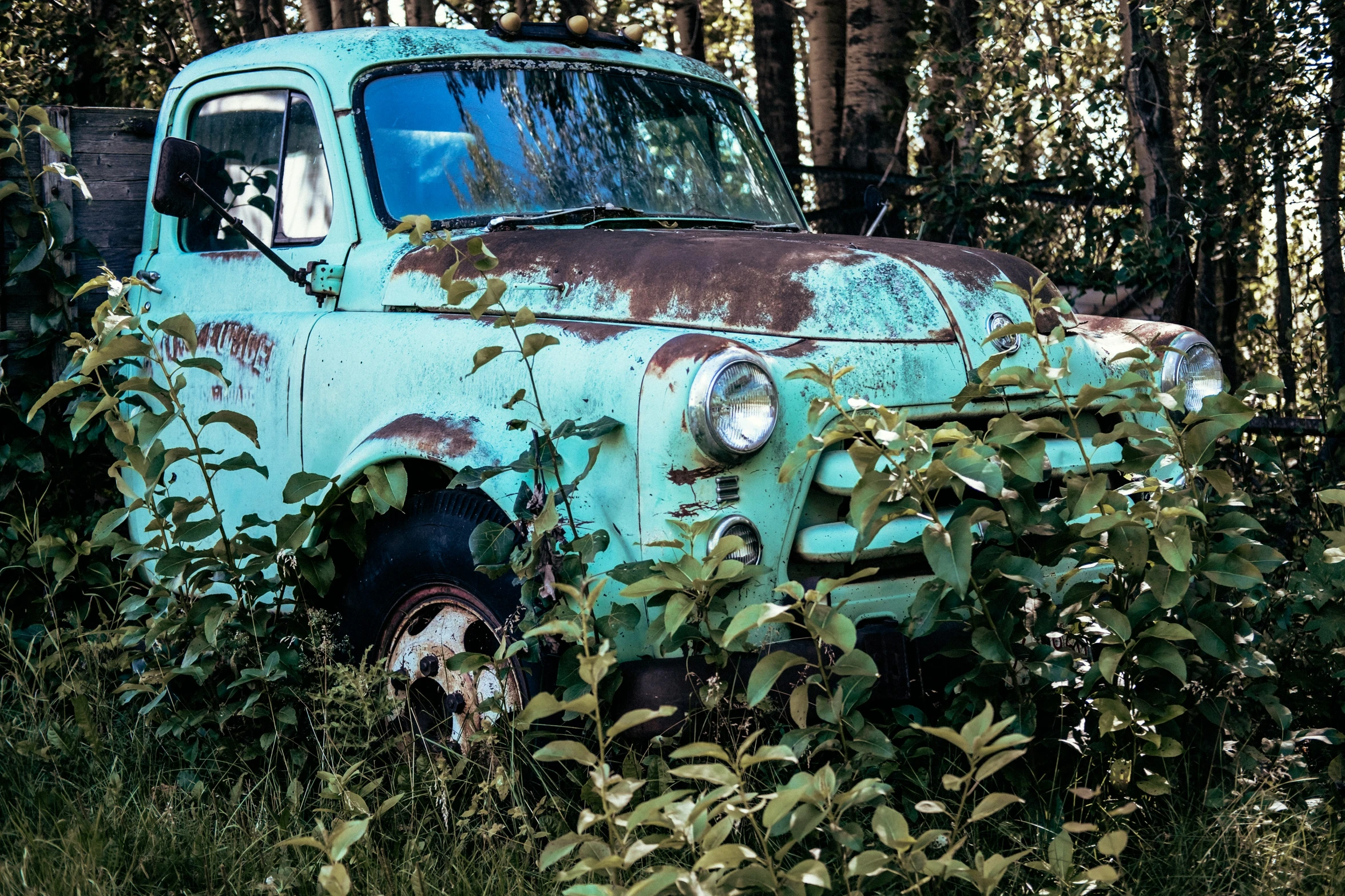 an old truck sitting in a forest with trees around