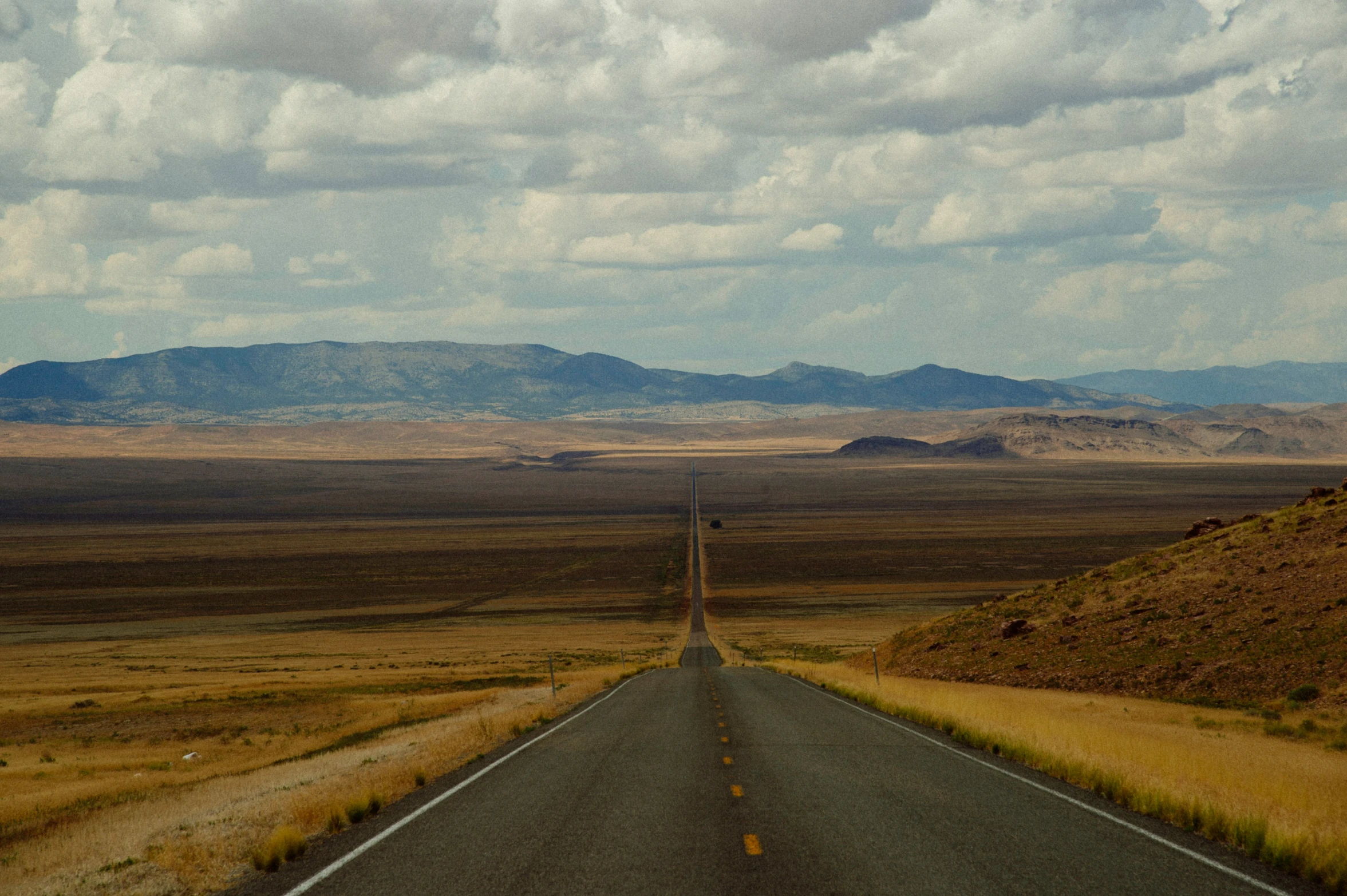 two empty open roads near some mountains under cloudy skies