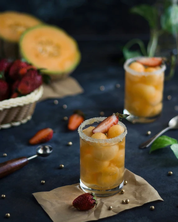 two cocktail glasses filled with fruit sit on a dark surface