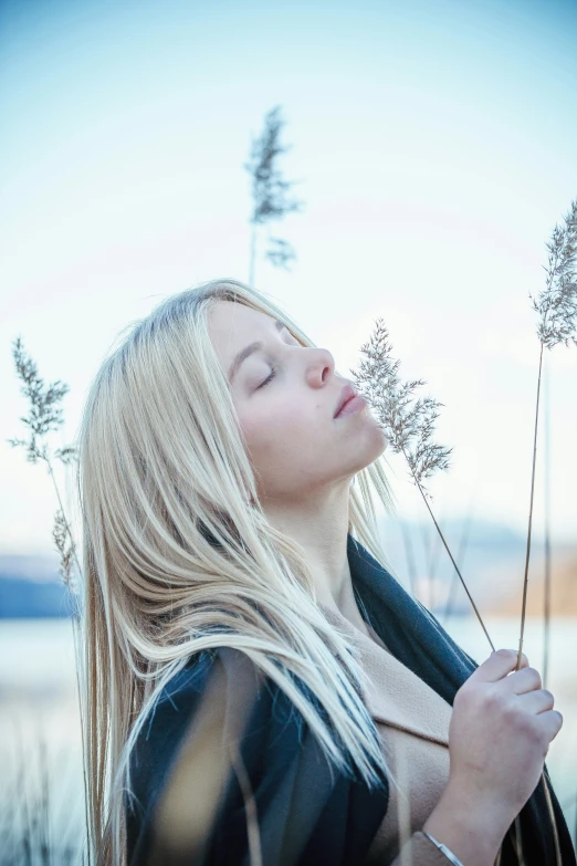 a woman with blonde hair standing in a field and looking at flowers