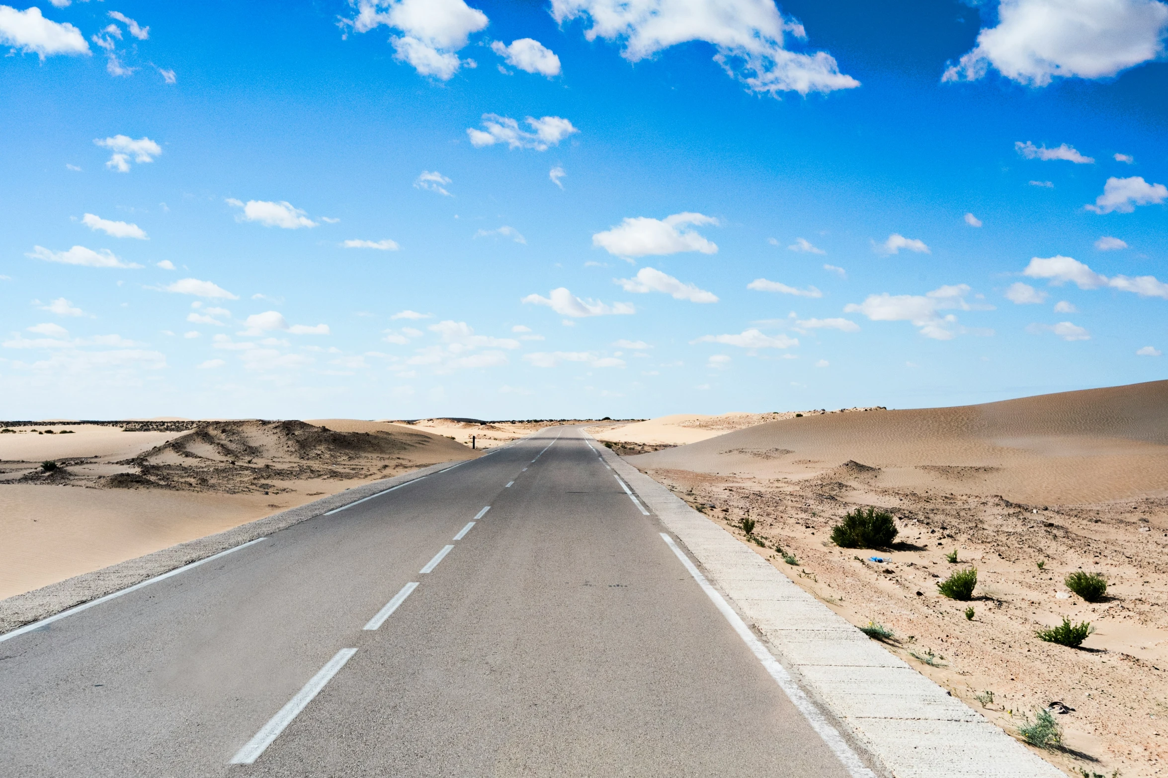 the road stretches through the desert through scrubland