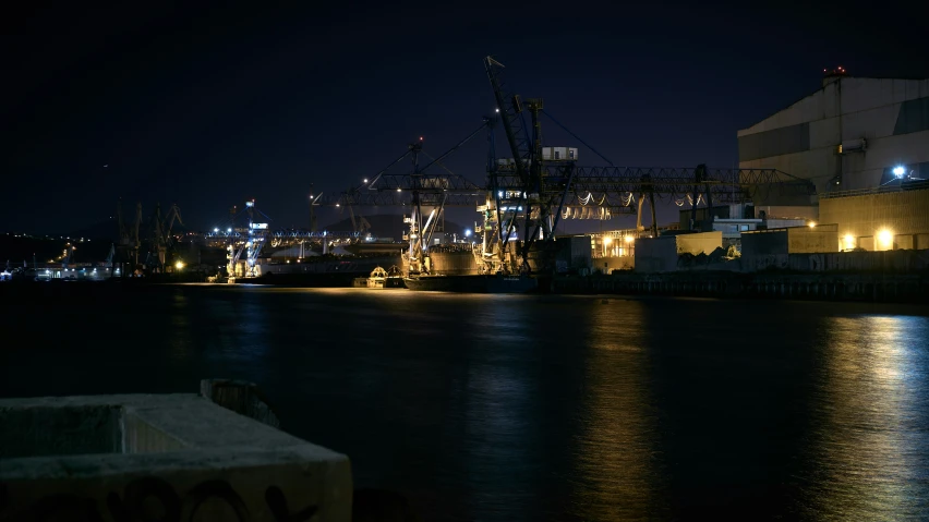 a cargo ship docked at night with lights reflected on the water
