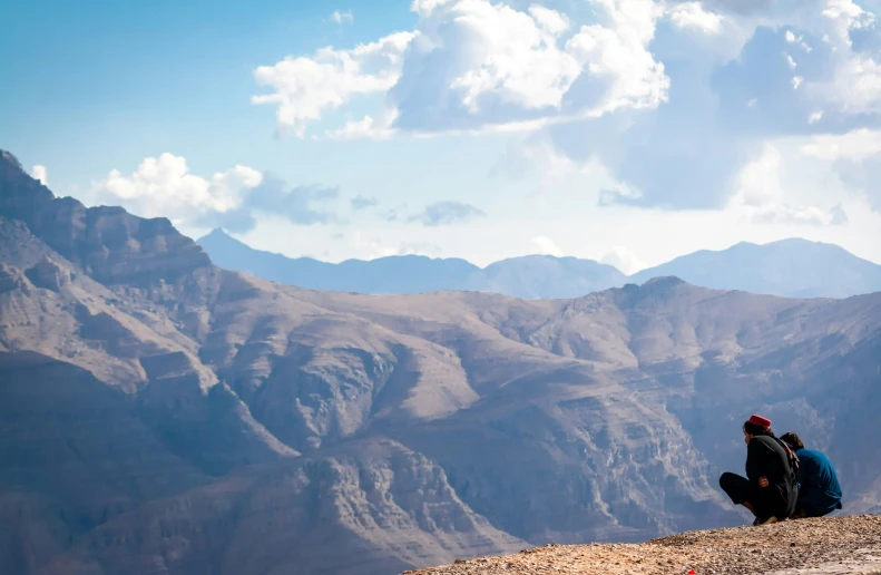 a man is sitting on a ledge looking over mountains