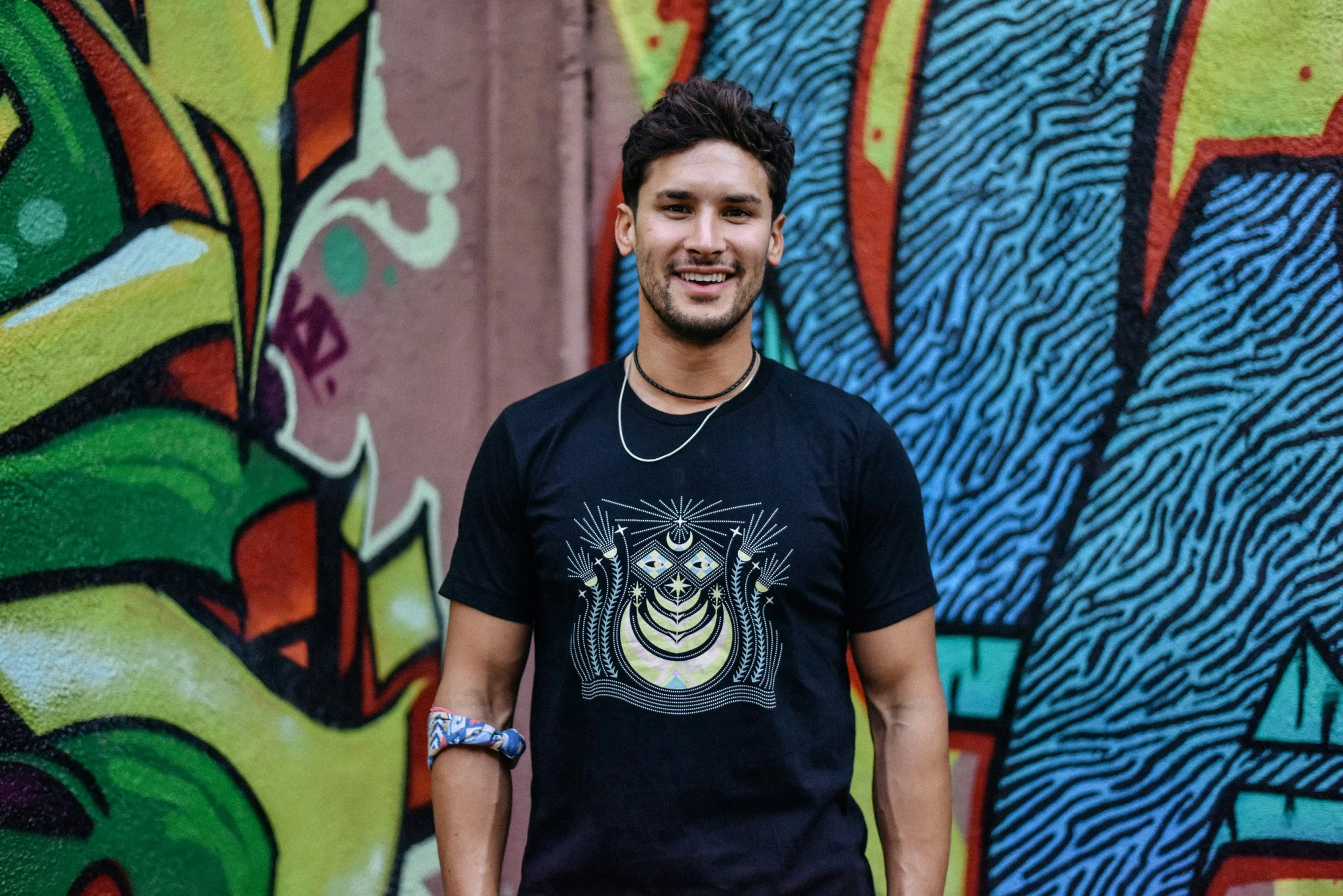 man in black shirt standing near wall with colorful graffiti