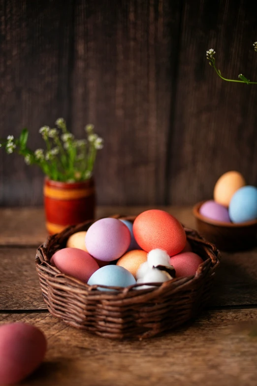 a basket filled with different colored eggs next to flowers