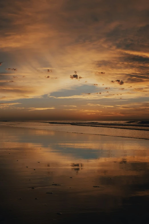 the sky is reflecting on the wet sand at sunrise