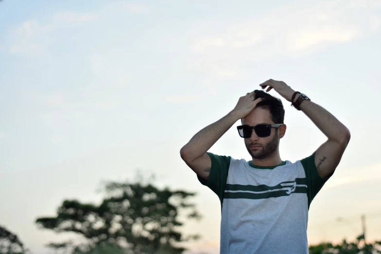 a man wearing sunglasses and a green t - shirt puts his hands behind his head