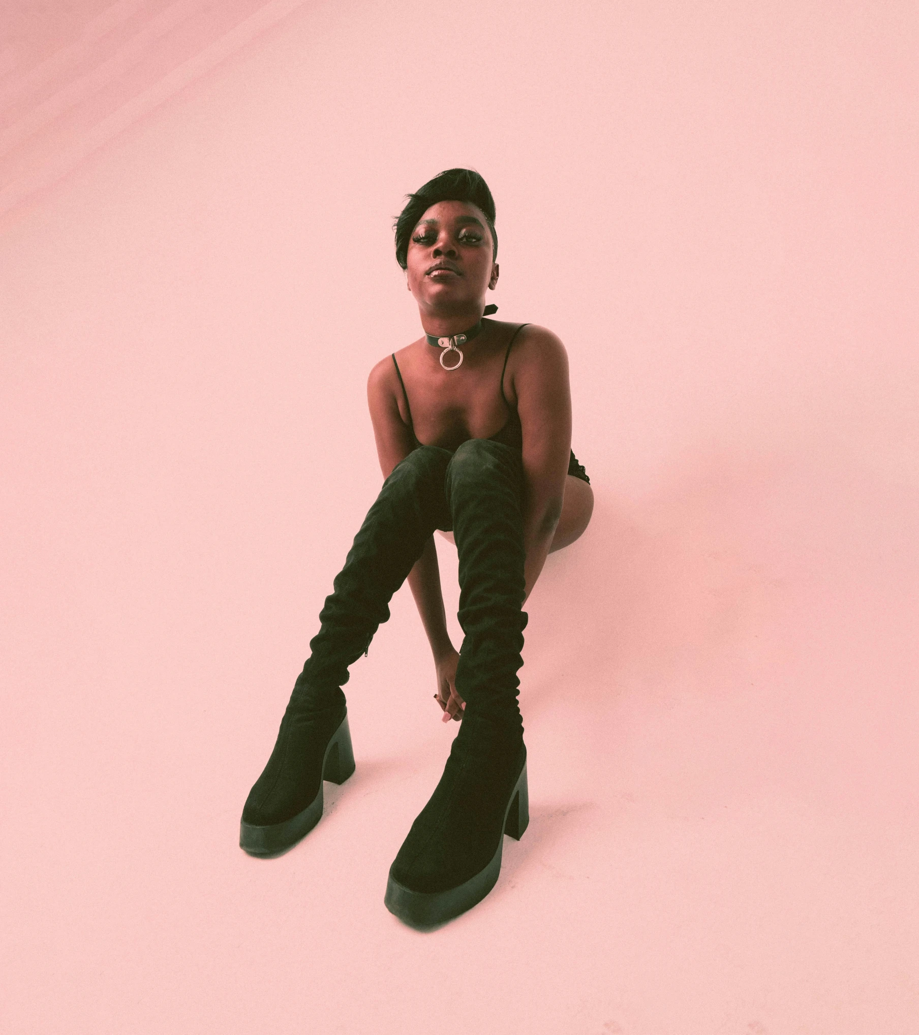 a black woman in boots sitting on pink background