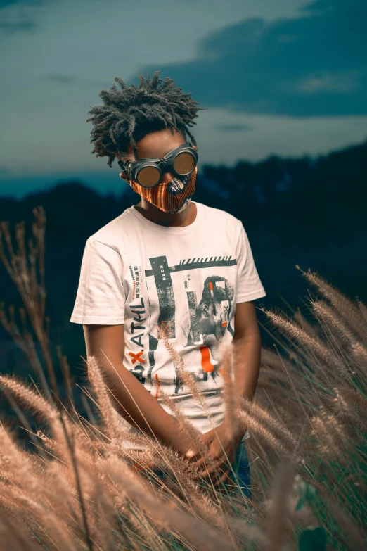 a black man with a mustache and a white shirt standing among brown grass