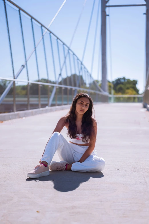 the woman is sitting on the ground by the bridge