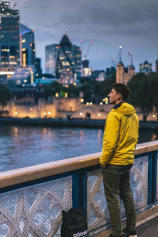 a man wearing yellow stands on the edge of a railing looking at a city skyline