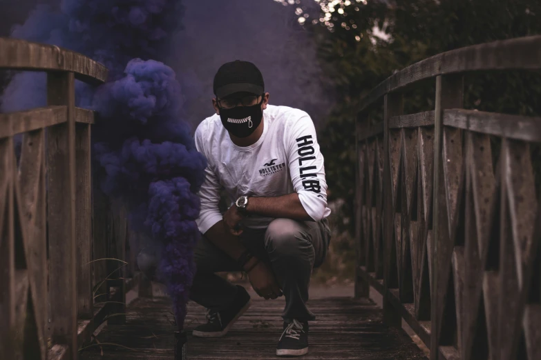 a man is kneeling on the edge of a bridge and a purple cloud of smoke