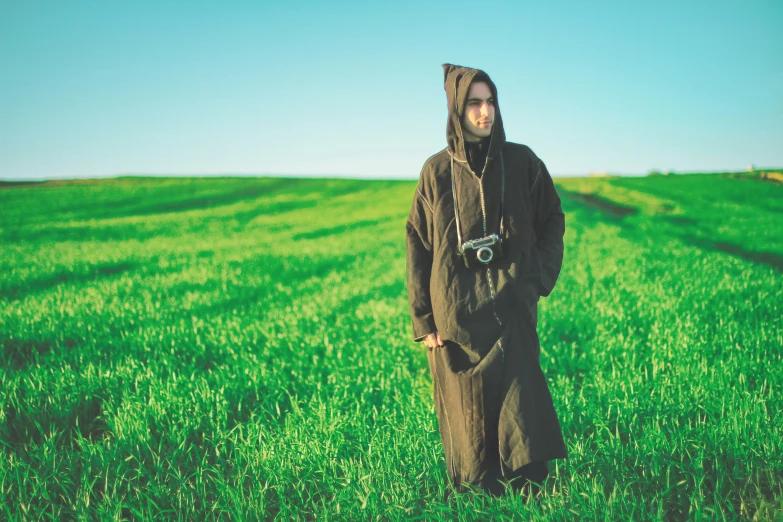 a man standing in a field of green grass wearing a hooded outfit