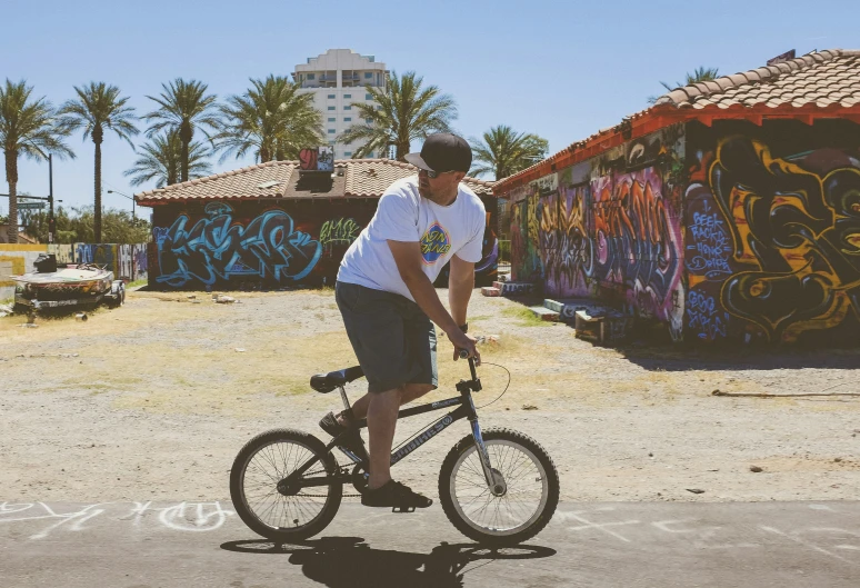 a  riding his bicycle in front of some graffiti covered structures