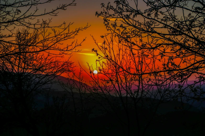 the sun setting in the sky over some trees