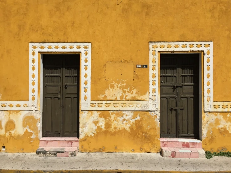 two brown doors are on this old yellow wall