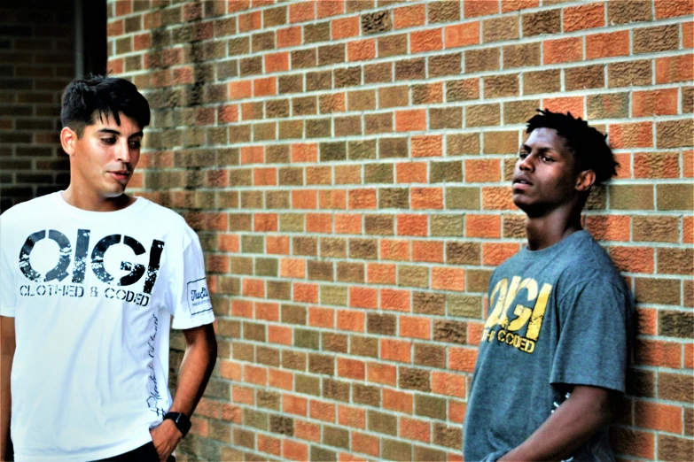 a group of two men standing next to a brick wall