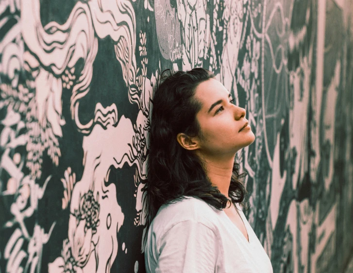 a young woman is leaning against the side of a wall with graffiti