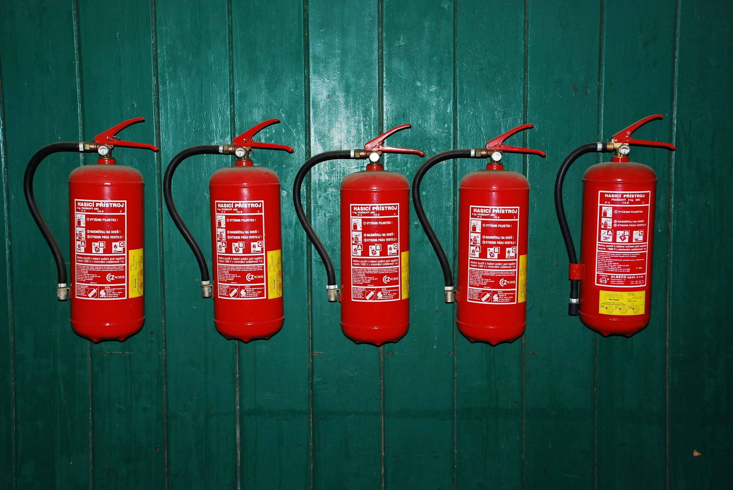 three red fire extinguishers line up against a green wall