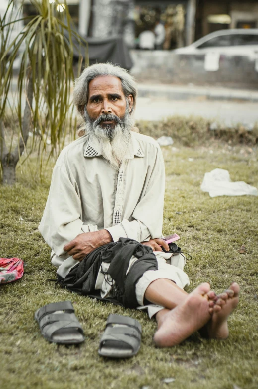 an old man sitting on the grass next to his shoes