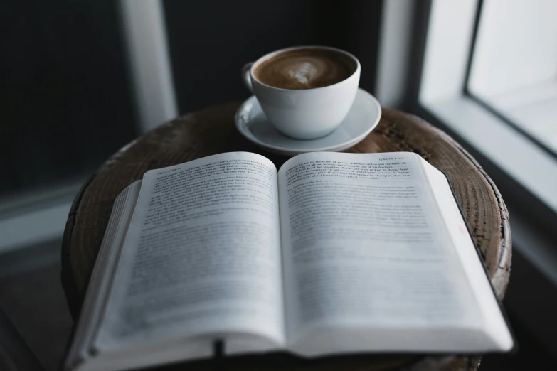 an open book and cup on a table with a mug of coffee