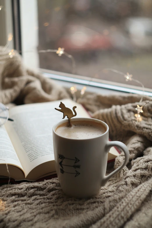 a white coffee cup with a brown dinosaur on top and a book near by