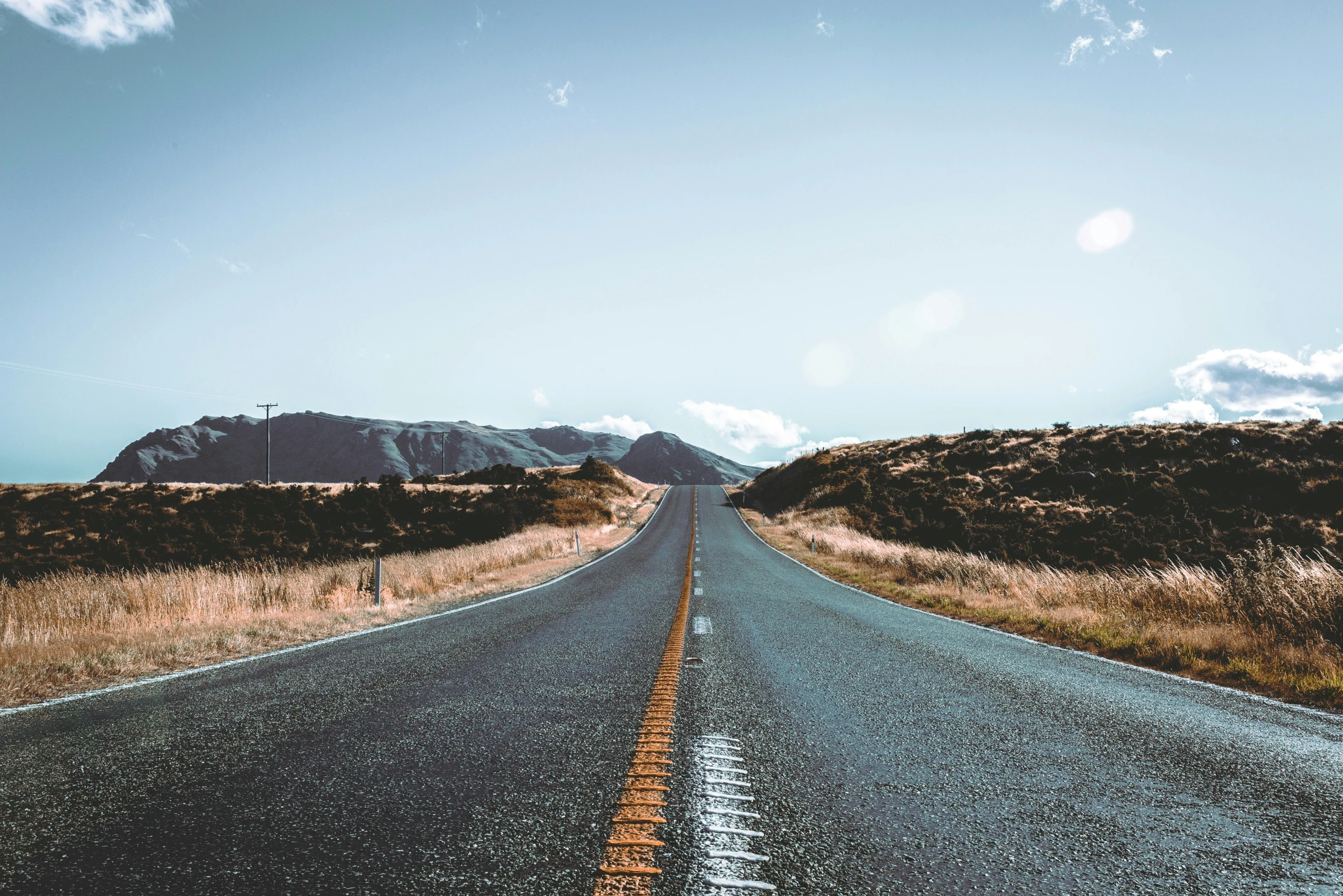 an empty, deserted road runs towards some mountains