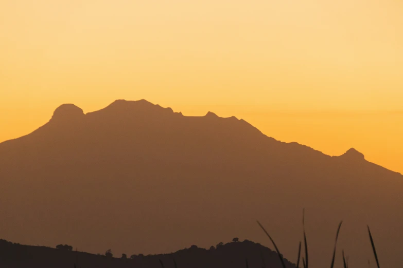 silhouette of a mountain with some trees on the foreground