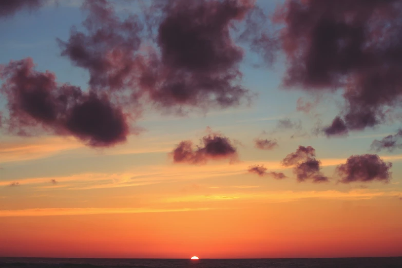 the sun is setting over the horizon with clouds