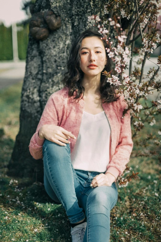 a young woman sits next to a cherry blossom tree