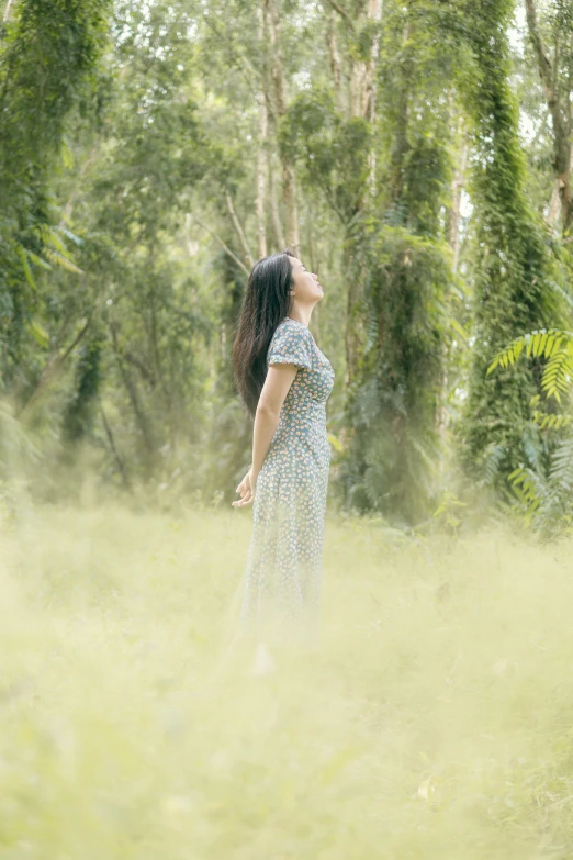 a woman standing in tall grass surrounded by trees