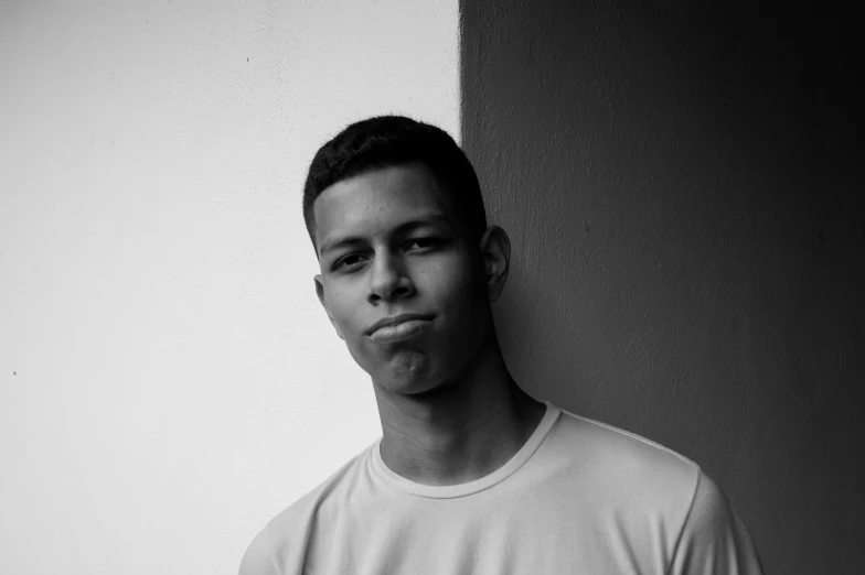 a young man wearing a white t - shirt poses in front of a wall