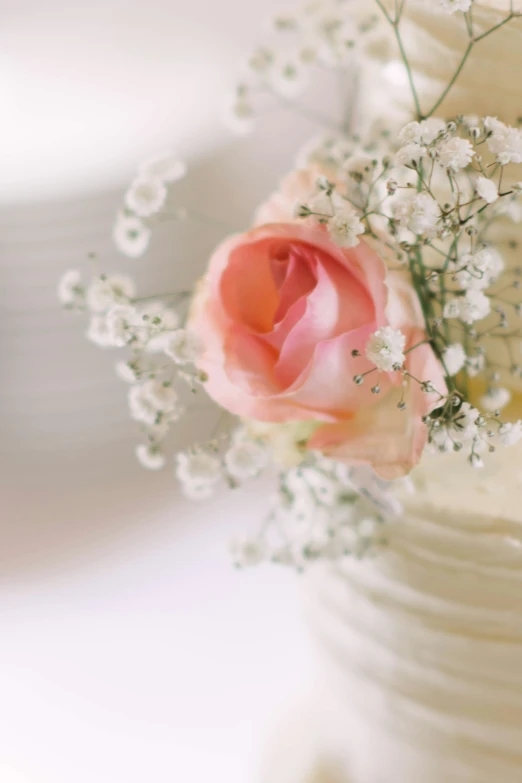 a white vase holding a pink flower and white baby's breath