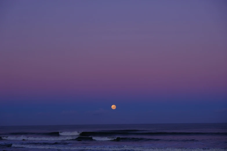 a beautiful full moon setting over the ocean