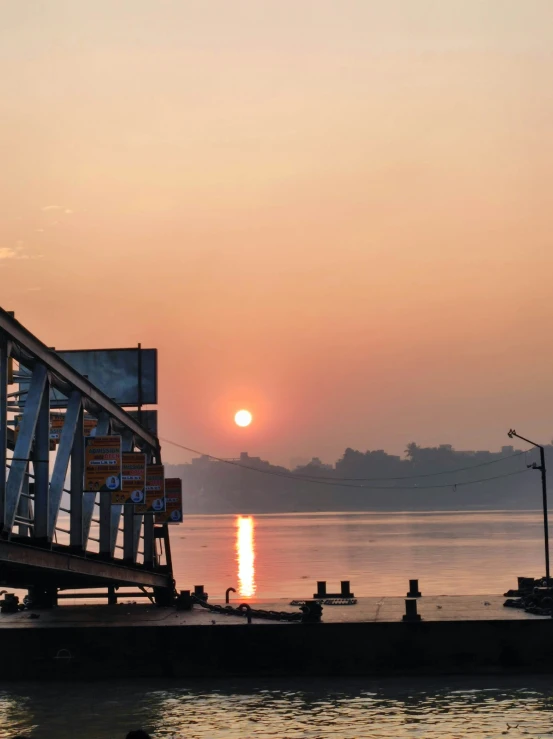 the sun is setting over water and the bridge is going to the shore