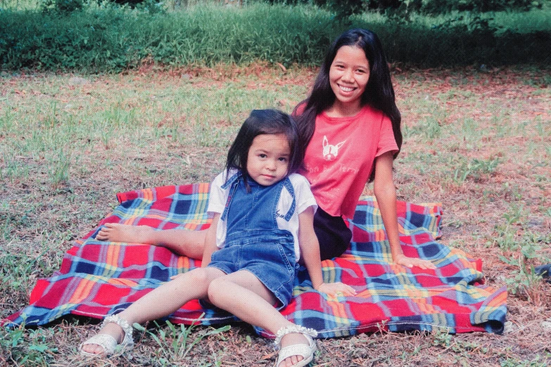 two girls sitting on a blanket together outside