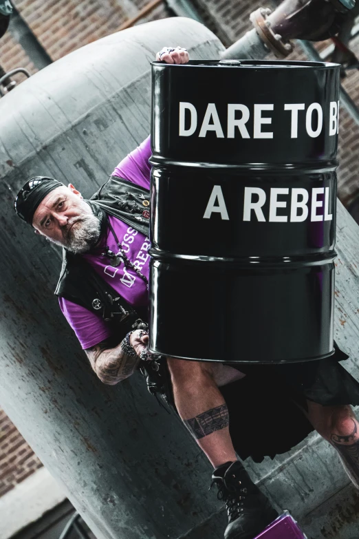 man in purple shirt and black shorts holding up a sign that says dare to be a rebel