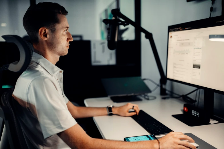 a man is using his phone and sitting in front of a monitor