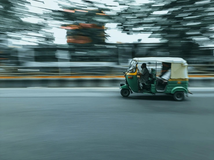 two people in a green and yellow vehicle traveling down the street