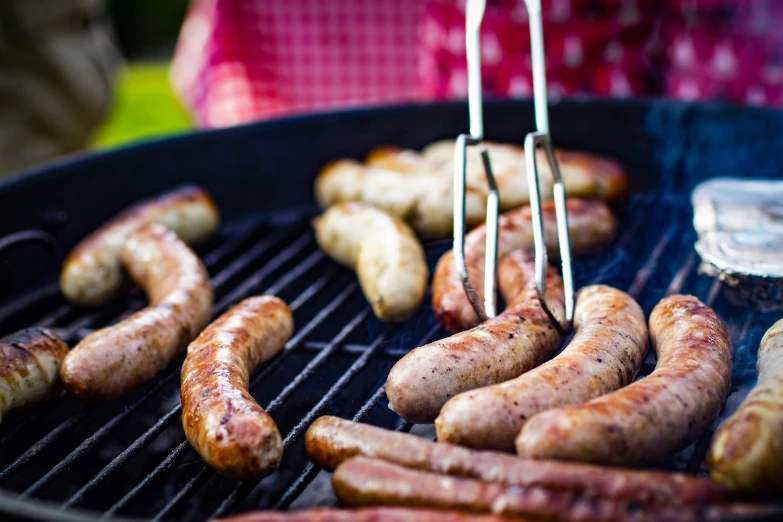 sausages being cooked on a grill with tongs