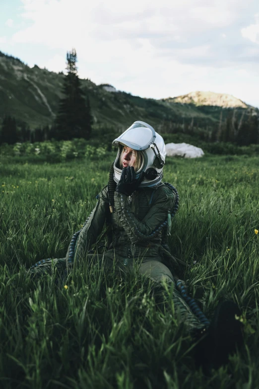 a person with a helmet is sitting in the grass talking on a phone